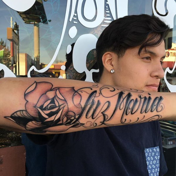 A gothic lettered rose tattoo on the arm